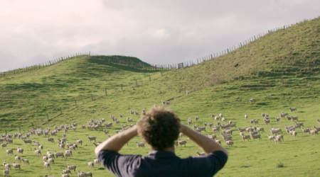 Rear view shot of a man looking out at his sheep in a New Zealand farm