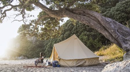 A young woman sits alone outside a tent on a beautiful morning in the Coromandel, New Zealand